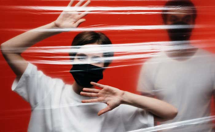 A man and a woman wearing masks look trapped behind a transparent plastic material