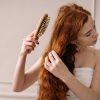 Red head woman with very long hair detangling her hair thanks to a wood hair brush