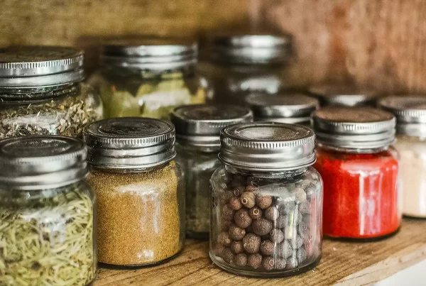 Spices and other natural ingredients stored in transparent bottles, sitting on a wooden shelf